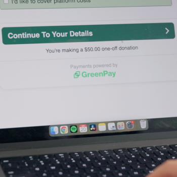 Laptop screen showing a donation checkout page with a "Continue to Your Details" button and "Payments powered by GreenPay" branding.